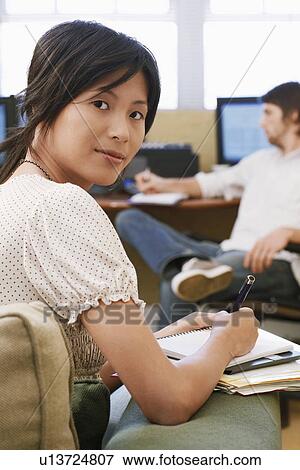Stock Photo - Woman Taking notes, man using computer in background.. Fotosearch