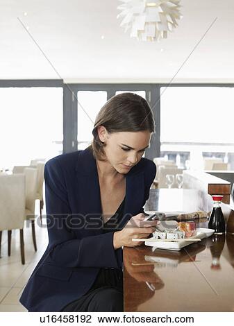 Stock Image - Woman text messaging in sushi restaurant. Fotosearch