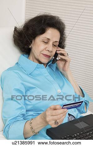 Stock Image - Woman Using Credit Card and Cell Phone to Make Online Purchase. Fotosearch
