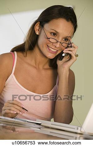 Stock Image - Woman Using Laptop and Cell Phone on kitchen counter. Fotosearch