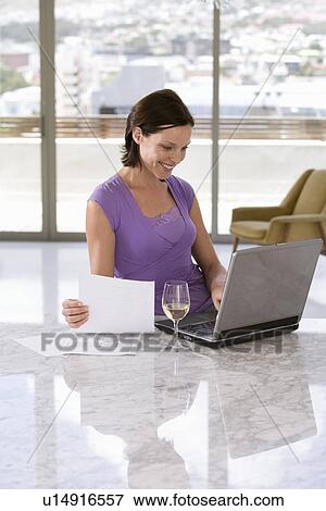 Woman using laptop and looking at paperwork, sitting at table, half length View Large Photo Image Stock Photo - Woman using laptop and looking at paperwork, sitting at table, half length. Fotosearch