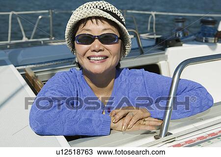 Stock Image - Woman wearing sunglasses on sailboat, smiling, (portrait). Fotosearch