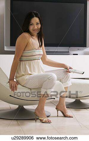 Stock Photograph - Woman with Remote Control sitting in front of large flat Screen Television, portrait. Fotosearch