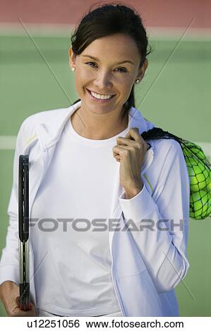 Stock Photograph - Woman with tennis balls and racket standing on tennis court, portrait. Fotosearch