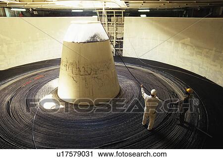 Stock Image - Workers feeding steel cable through hole in ceiling. Fotosearch