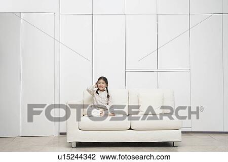 Stock Image - Young, barefoot Girl sitting cross-legged Sofa. Fotosearch
