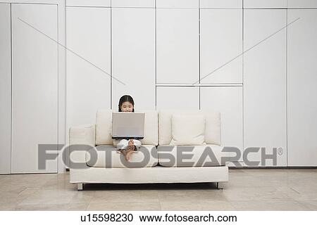 Stock Image - Young, barefoot Girl Using Laptop on Sofa. Fotosearch