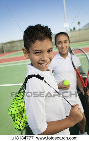 Stock Photo - Young boy and girl with tennis equipment on tennis court, focus on boy, portrait. Fotosearch