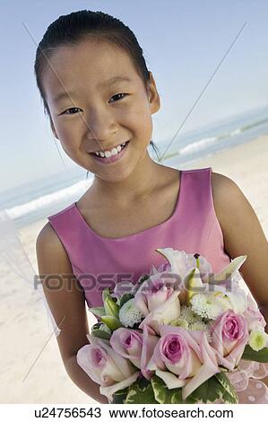 Stock Image - Young Bridesmaid with flowers on beach, (portrait). Fotosearch