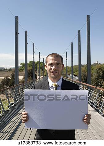 Stock Image - Young business man standing on bridge holding papers. Fotosearch