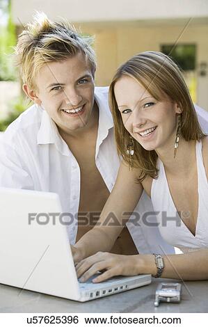Young couple sitting at backyard table using laptop, portrait View Large Photo Image Stock Photograph - Young couple sitting at backyard table using laptop, portrait. Fotosearch