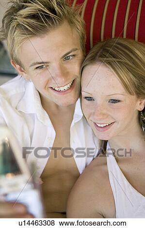 Stock Photo - Young couple taking camera phone picture of selves on sofa, high angle view. Fotosearch