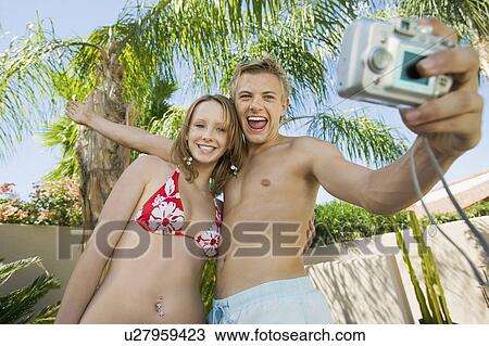 Stock Image - Young couple taking photo of themselves, low angle view. Fotosearch