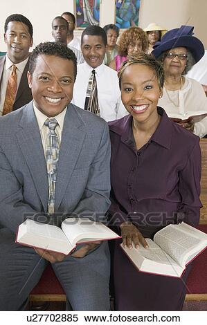 Stock Photography - Young couple with Bibles sitting on church pews, portrait. Fotosearch