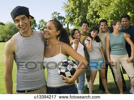 Stock Photo - Young couple with woman holding soccer ball, group of friends in background.. Fotosearch