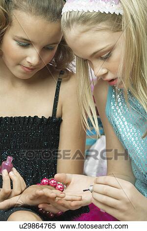 Stock Photography - Young girl applying nail polish to friends fingernails. Fotosearch