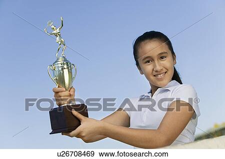 Stock Photo - Young girl at net on tennis court holding trophy, portrait, low angle view. Fotosearch