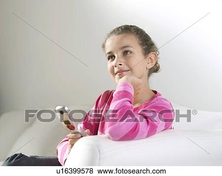 Stock Photo - Young Girl leaning on arm of sofa, hand on chin, holding phone, daydreaming. Fotosearch