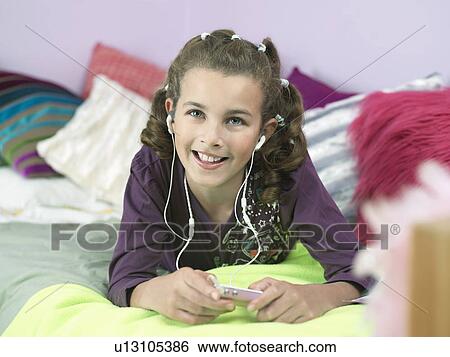 Stock Photograph - Young Girl lying on front, Listening to MP3 Player on bed. Fotosearch