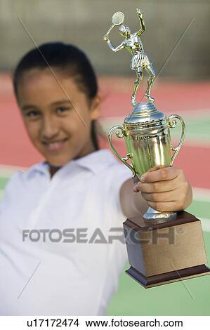 Picture - Young girl on tennis court holding trophy, focus on trophy. Fotosearch