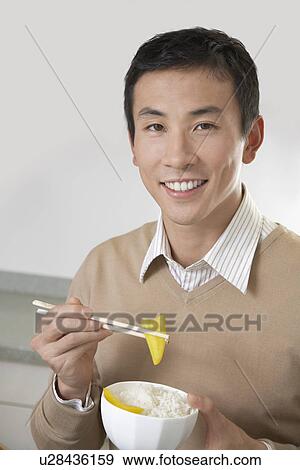 Stock Photo - Young Man Eating Rice and Peppers with chopsticks. Fotosearch