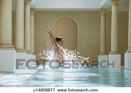 Stock Photo - Young man jumping out of water in swimming pool, side view. Fotosearch