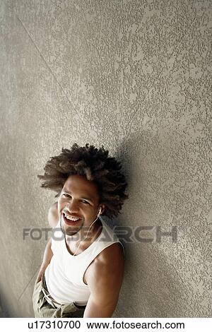 Young man leaning against wall listening to music through headphones, portrait View Large Photo Image Stock Image - Young man leaning against wall listening to music through headphones, portrait. Fotosearch