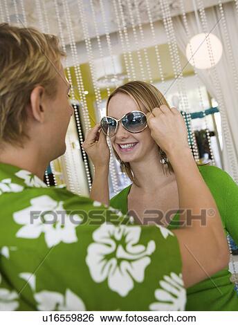 Young man putting sunglasses on girlfriend in clothing store View Large Photo Image Stock Photograph - Young man putting sunglasses on girlfriend in clothing store. Fotosearch