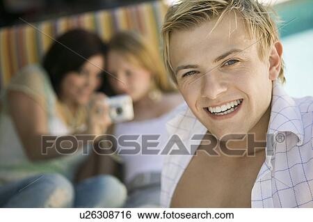 Young man sitting on patio smiling, portrait View Large Photo Image Stock Photograph - Young man sitting on patio smiling, portrait. Fotosearch