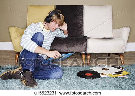 Stock Image - Young Man sitting on shag rug, leaning on sofa, listening to records. Fotosearch