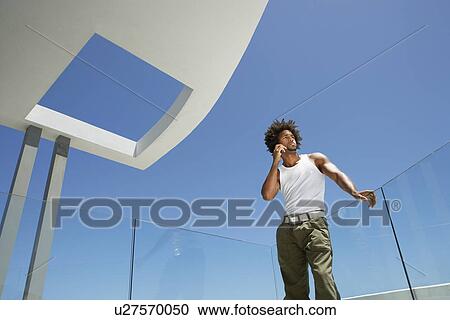 Young man using mobile phone on balcony, portrait, low angle view View Large Photo Image Stock Image - Young man using mobile phone on balcony, portrait, low angle view. Fotosearch