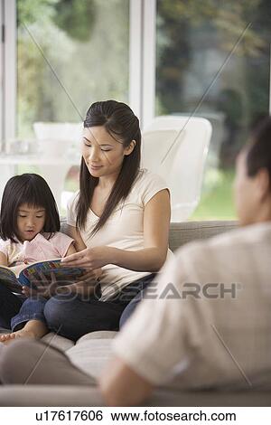 Stock Photograph - Young Mother Sitting on sofa, Holding Page of Coloring Book for Daughter. Fotosearch
