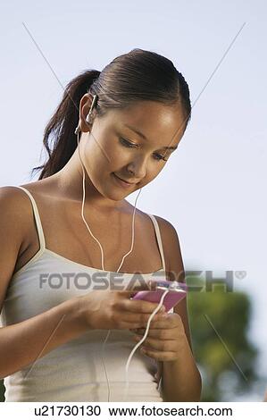 Stock Image - Young Woman listening to portable music player outdoors.. Fotosearch