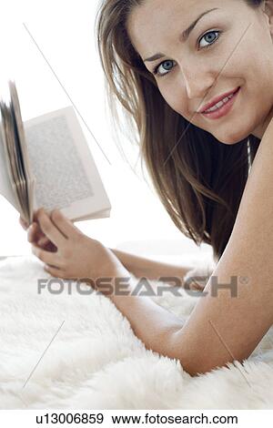 Stock Photo - Young woman lying down, holding book, portrait, close-up. Fotosearch