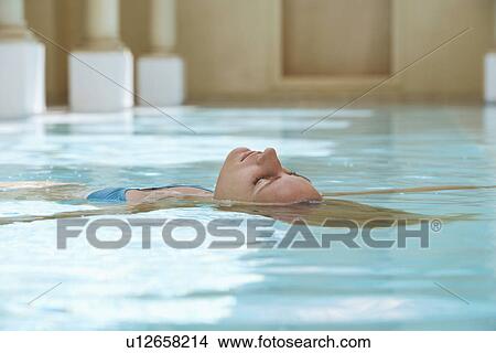 Picture - Young woman lying on back in swimming pool, portrait. Fotosearch