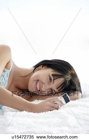 Stock Photography - Young woman lying on bed using mobile phone, portrait. Fotosearch