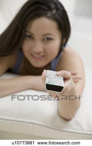 Stock Image - Young Woman lying on Couch using Remote Control, personal perspective, focus on remote control. Fotosearch