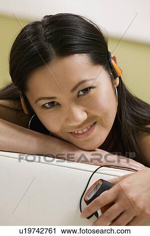 Stock Image - Young Woman lying on sofa Listening to MP3 Player, portrait, close up. Fotosearch