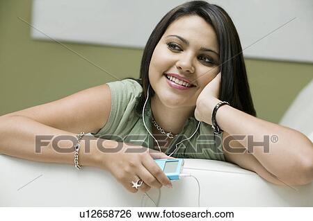 Stock Photograph - Young woman lying on sofa listening to MP3 player, close up, front view. Fotosearch