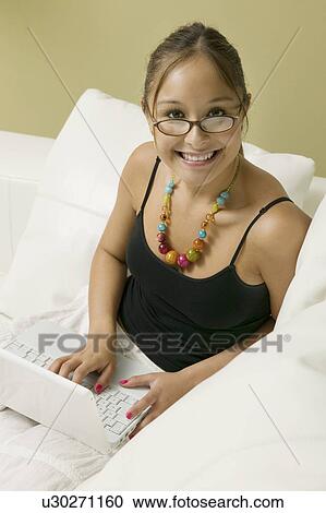 Stock Image - Young woman on sofa using laptop, portrait, high angle view. Fotosearch