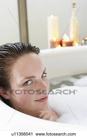 Stock Image - Young woman relaxing in bubble bath, close-up. Fotosearch