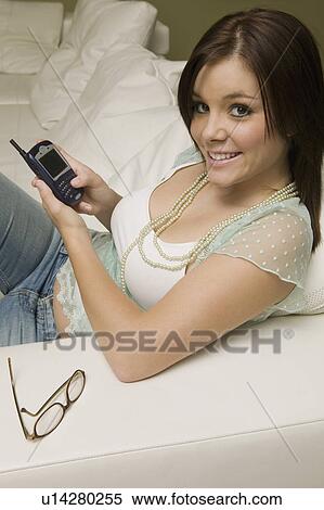 Stock Photography - Young woman sitting on sofa with mobile phone, portrait, high angle view. Fotosearch