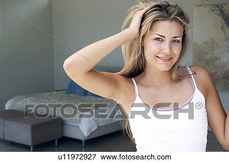 Stock Photo - Young woman standing in bedroom, tousling hair, portrait. Fotosearch
