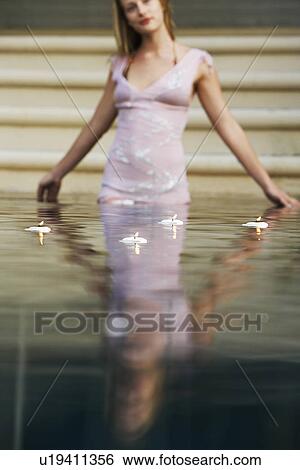 Stock Photograph - Young woman surrounded by floating candles standing in swimming pool, portrait. Fotosearch