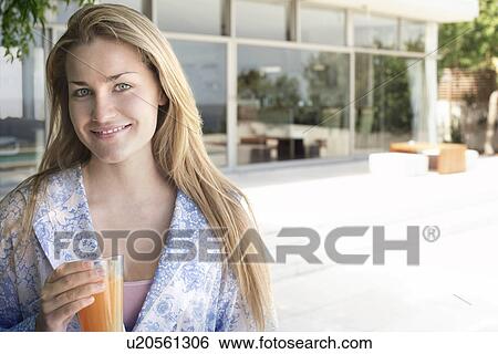Stock Photograph - Young woman wearing bathrobe, holding glass of juice outdoors, portrait. Fotosearch