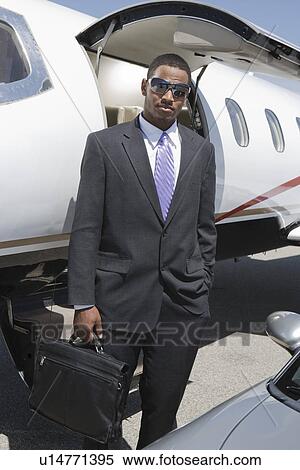 Stock Photography - African-American businessman standing in front of private airplane and car.. Fotosearch