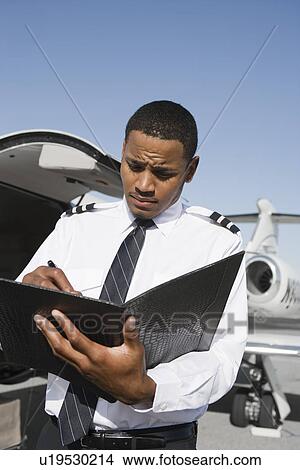 Picture - Airline pilot standing and making notes in front of airplane.. Fotosearch