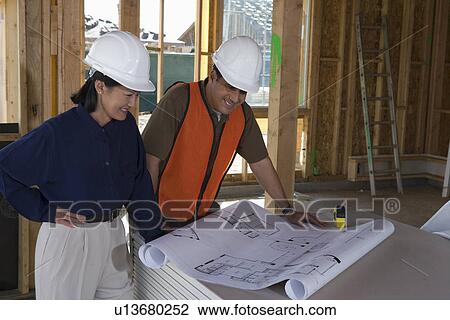 Architect and construction worker looking at blueprints inside half constructed house View Large Photo Image Stock Image - Architect and construction worker looking at blueprints inside half constructed house. Fotosearch