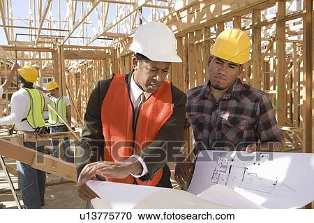 Stock Image - Architect and construction worker looking at blueprints. Fotosearch