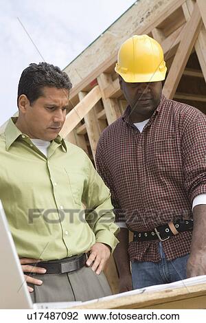 Stock Image - Architect and construction worker examining structure on construction site. Fotosearch